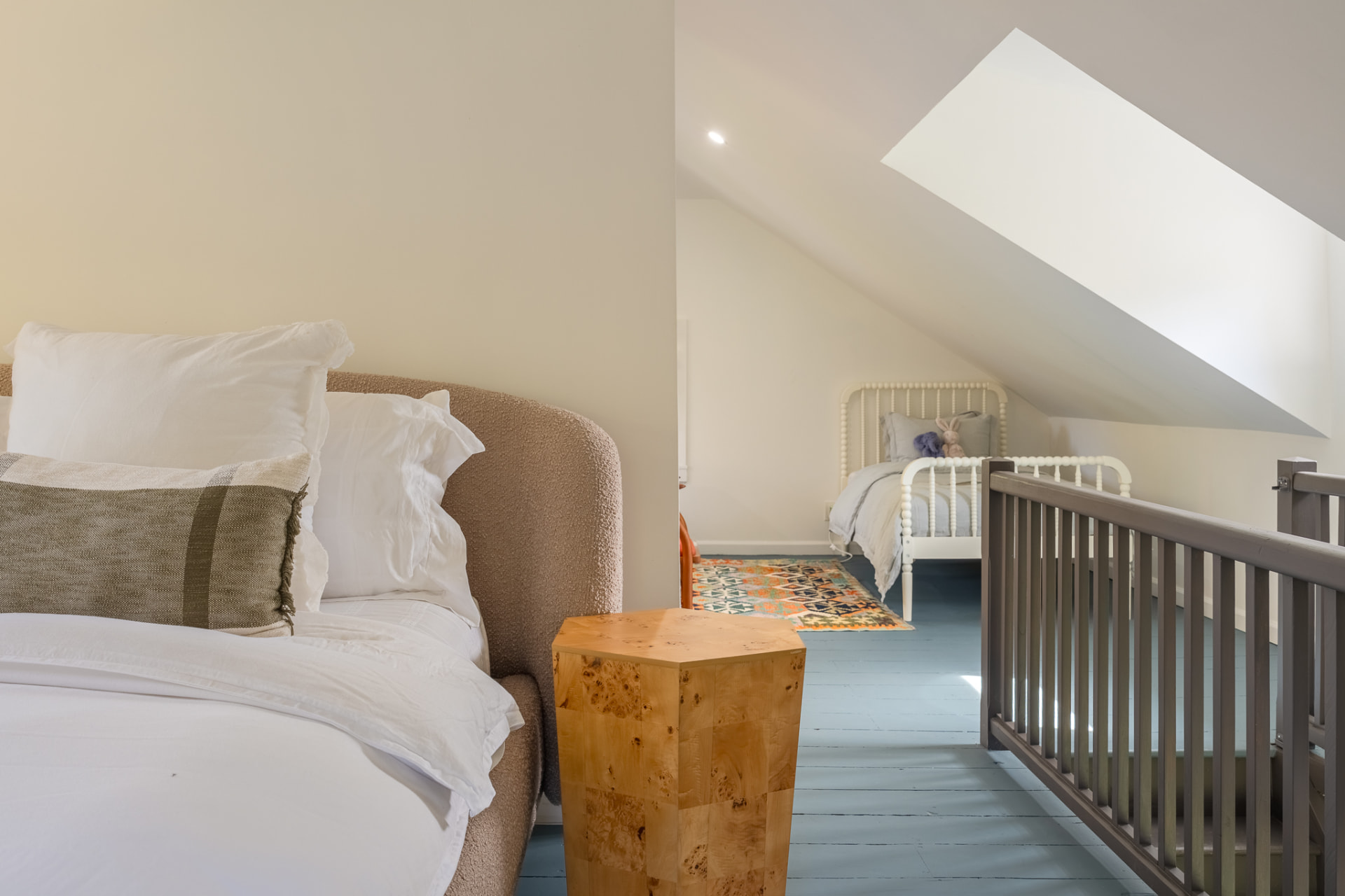 The Gatehouse loft bedroom, with a bouclé-headed bed under the skylight and a twin bed in the dormer nook beyond