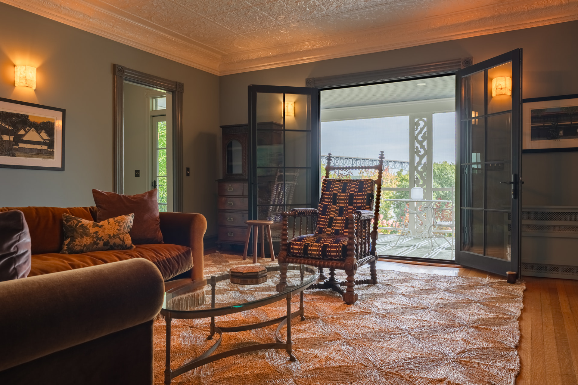 The Main House living room, with a brown velvet sofa and open French doors to the porch, the river and bridge beyond