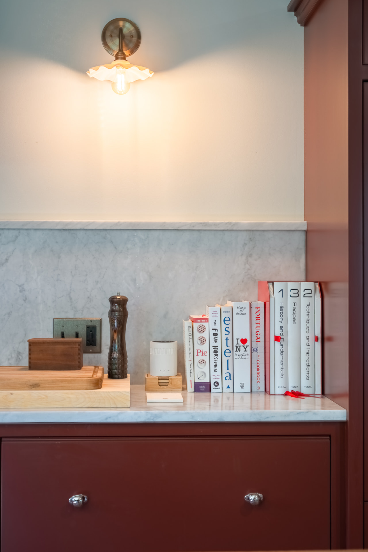 Marble kitchen counter with cookbooks under a brass sconce